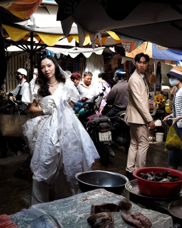 A bride and groom stand among the fish basins of a Saigon wet market — photograph by Luke Neville