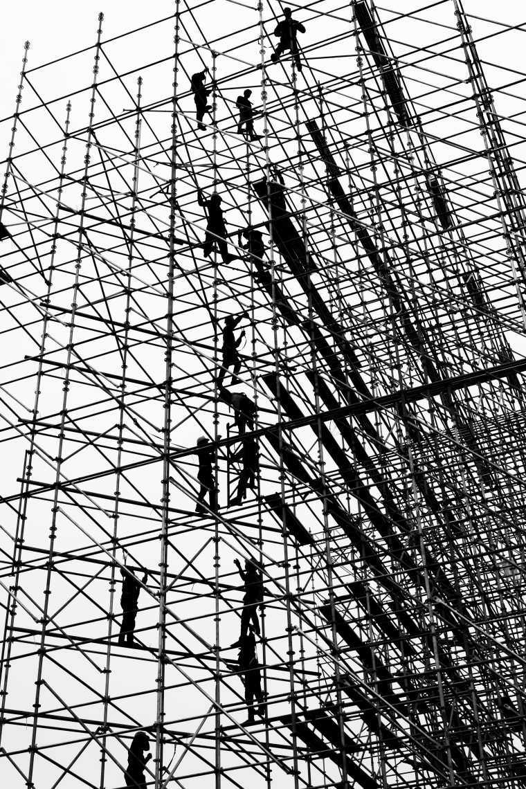 Hoàn Kiếm, 2026 — a dense black-and-white lattice of scaffolding with small figures climbing inside it — Lâm Xuân Tùng