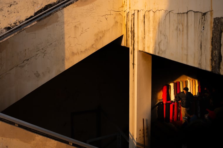 Đồng Xuân, 2024 — a bare concrete stairwell, its wall cracked and stained, with a small red-lit doorway at the far side — Lâm Xuân Tùng