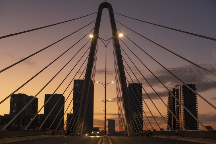 A cable-stayed bridge fans out against an orange dusk sky, a lone van crossing beneath its lights — Paul Evan Green