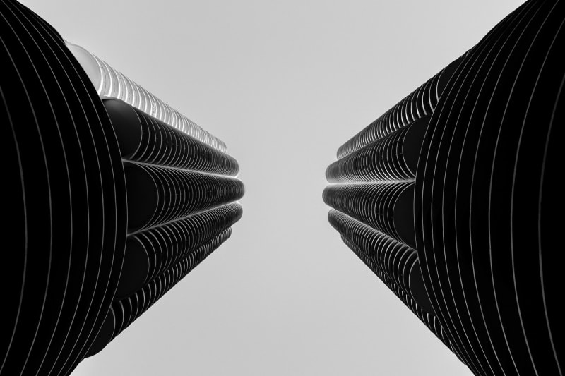 Black-and-white abstract of two high-rise facades converging toward a bright centre of sky