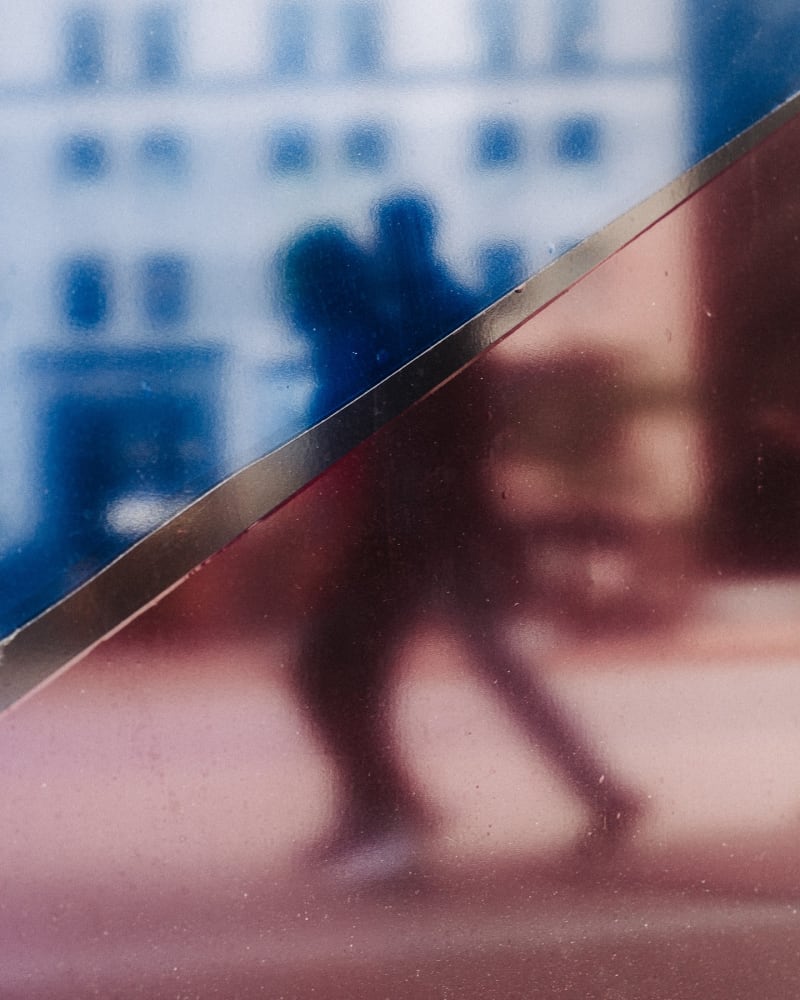 Abstract frame of a walking figure reflected in a polished red surface beneath a blue glass facade
