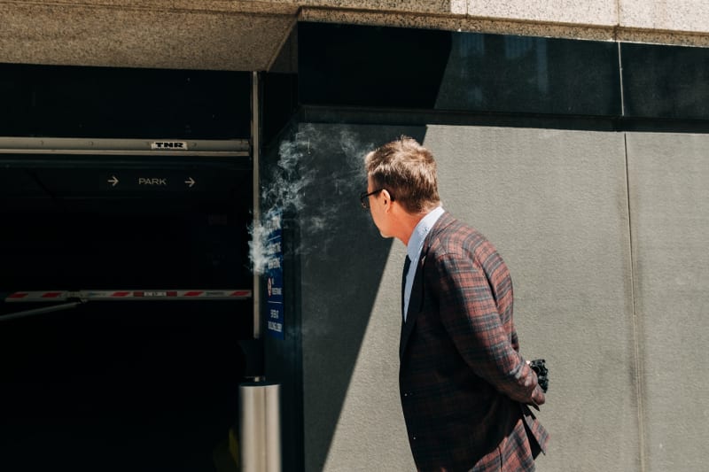 A man in a plaid blazer exhales cigarette smoke while walking past the corner of a downtown Chicago building