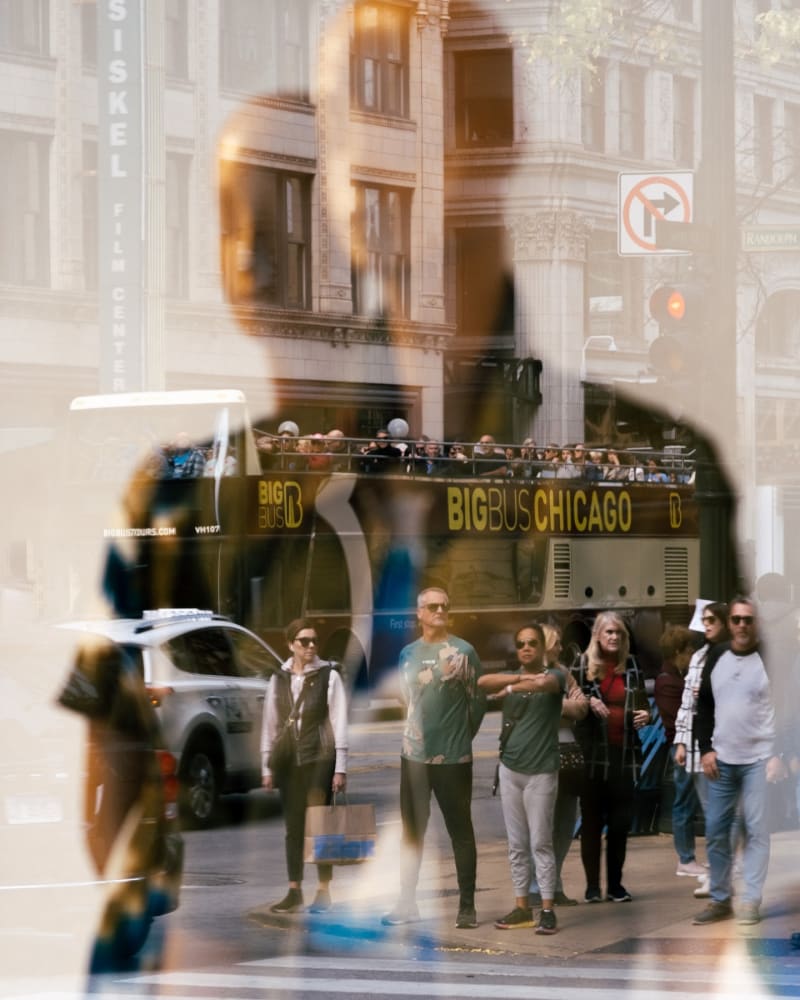 Layered storefront window reflection showing a Chicago sightseeing bus and a group of pedestrians overlapping