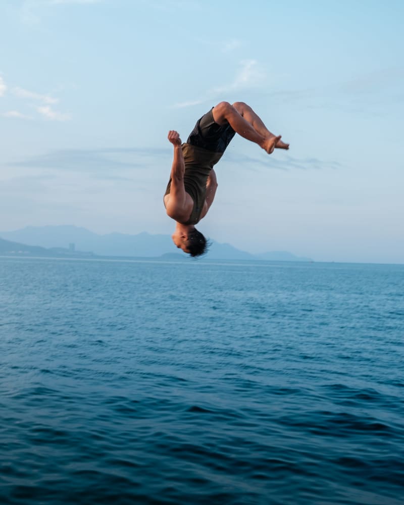 A swimmer mid-backflip above the sea, mountains on the far shore
