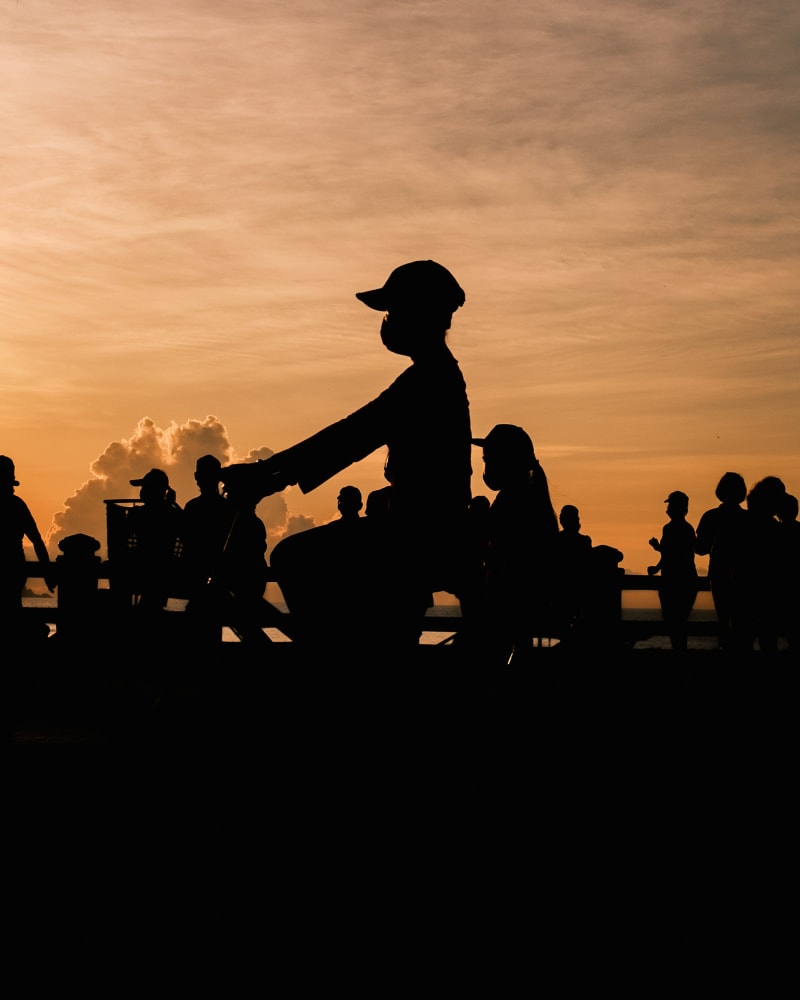 Silhouetted figures and a cyclist along a seafront railing against a burning orange sunset in Nha Trang