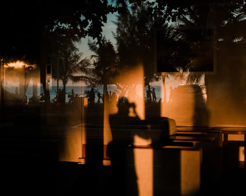 Palms and a seafront promenade seen through a window, overlaid with warm orange reflections