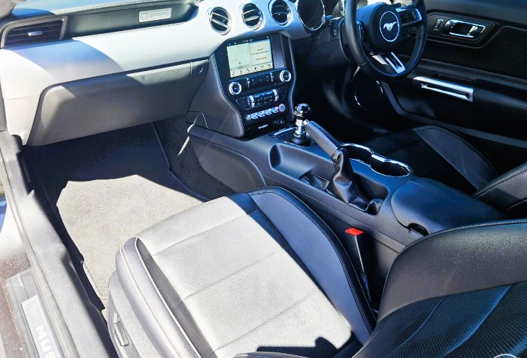 Ford Mustang driver interior — pony badge on steering wheel, manual shifter, alloy pedals