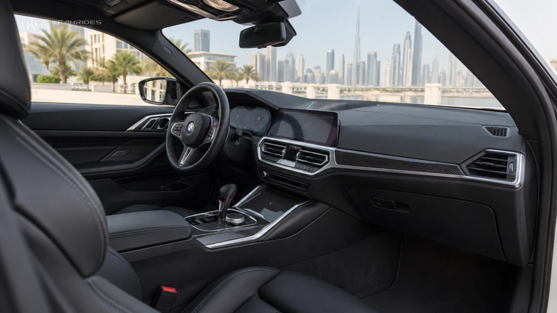 Left-hand-drive BMW M4 cockpit with black sport seats and daylight across the centre console