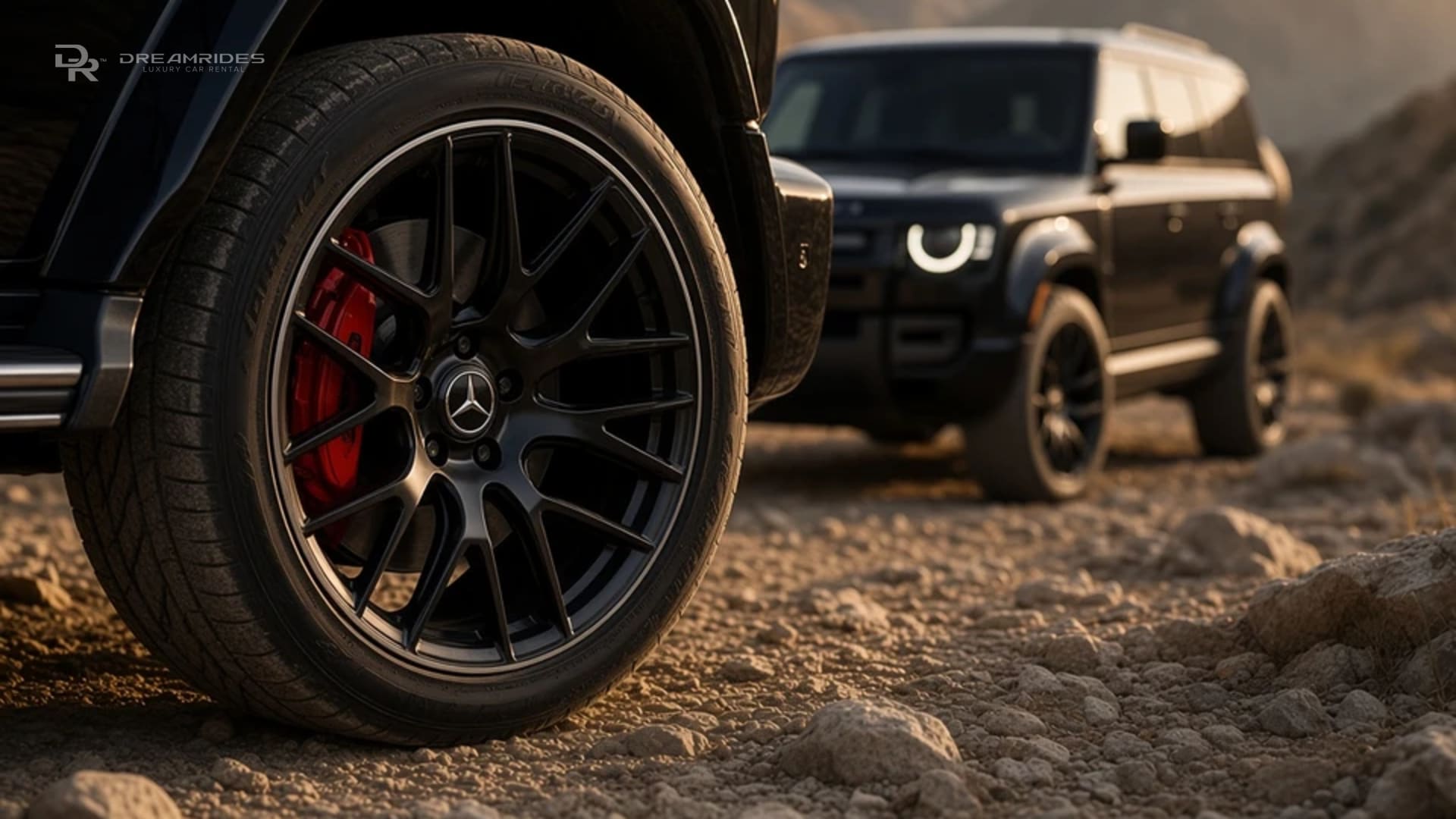 Close-up of a black G63 alloy wheel with red brake caliper beside a black Defender 110 on a rocky mountain track