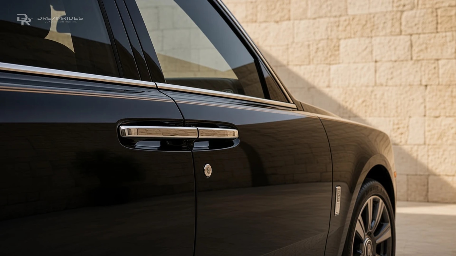 Daylight close-up of a black Rolls-Royce door handle and coachline against pale resort stone