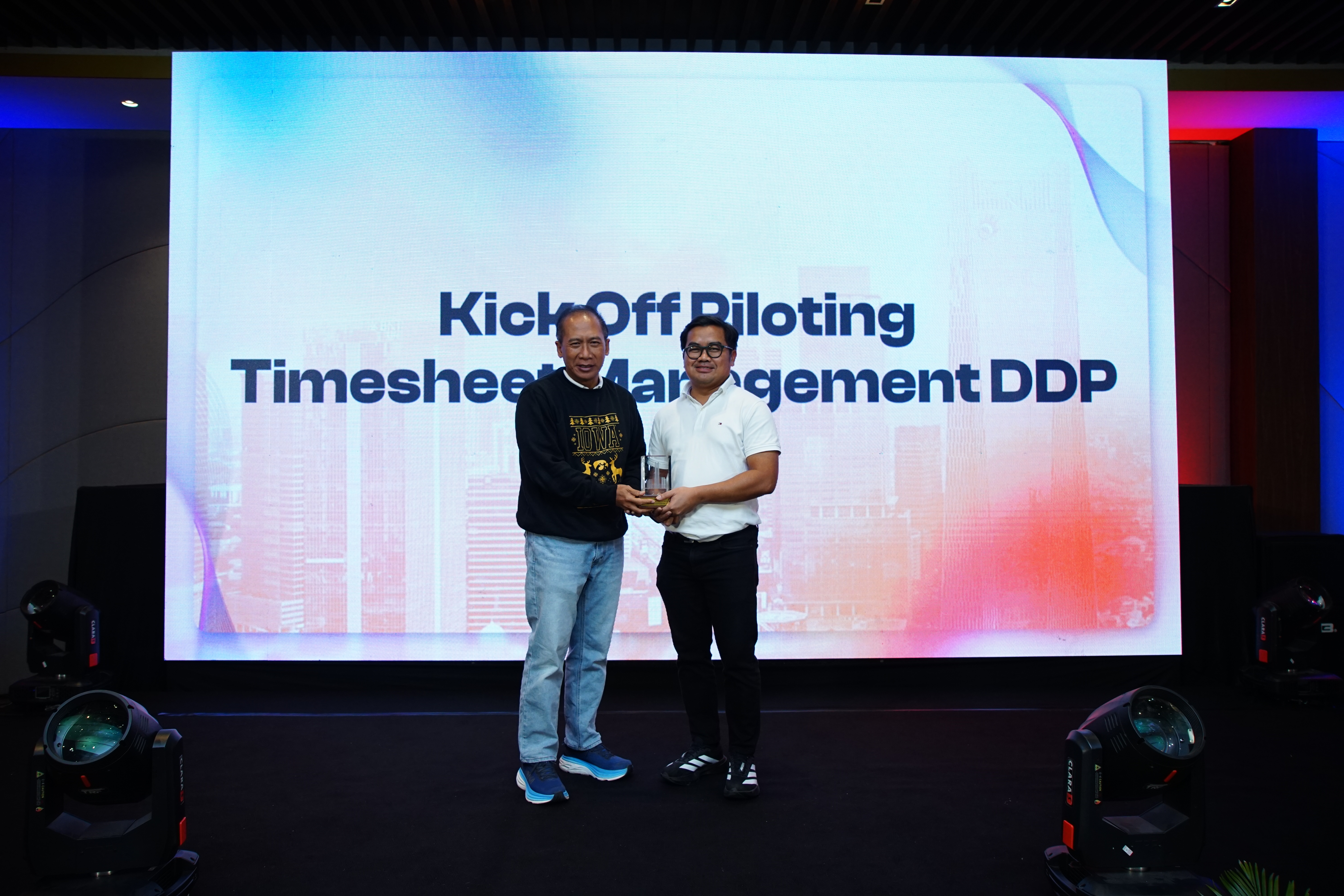 Kick Off Piloting Timesheet Management DDP — penyerahan penghargaan di atas panggung dengan slide judul acara di layar belakang