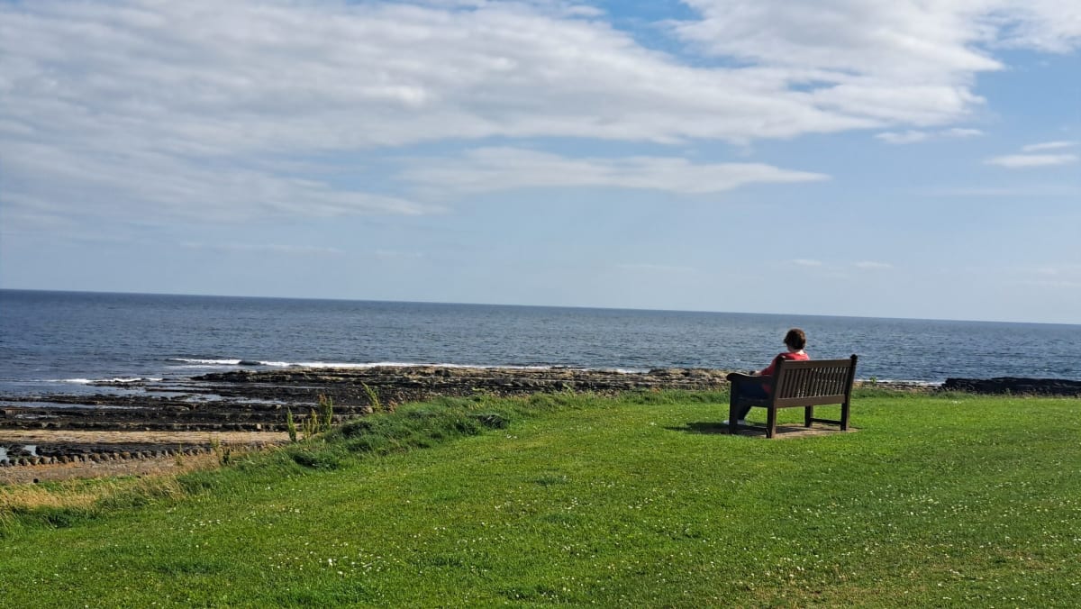 Lady siting on a bench looking out on Raad ny Foillan