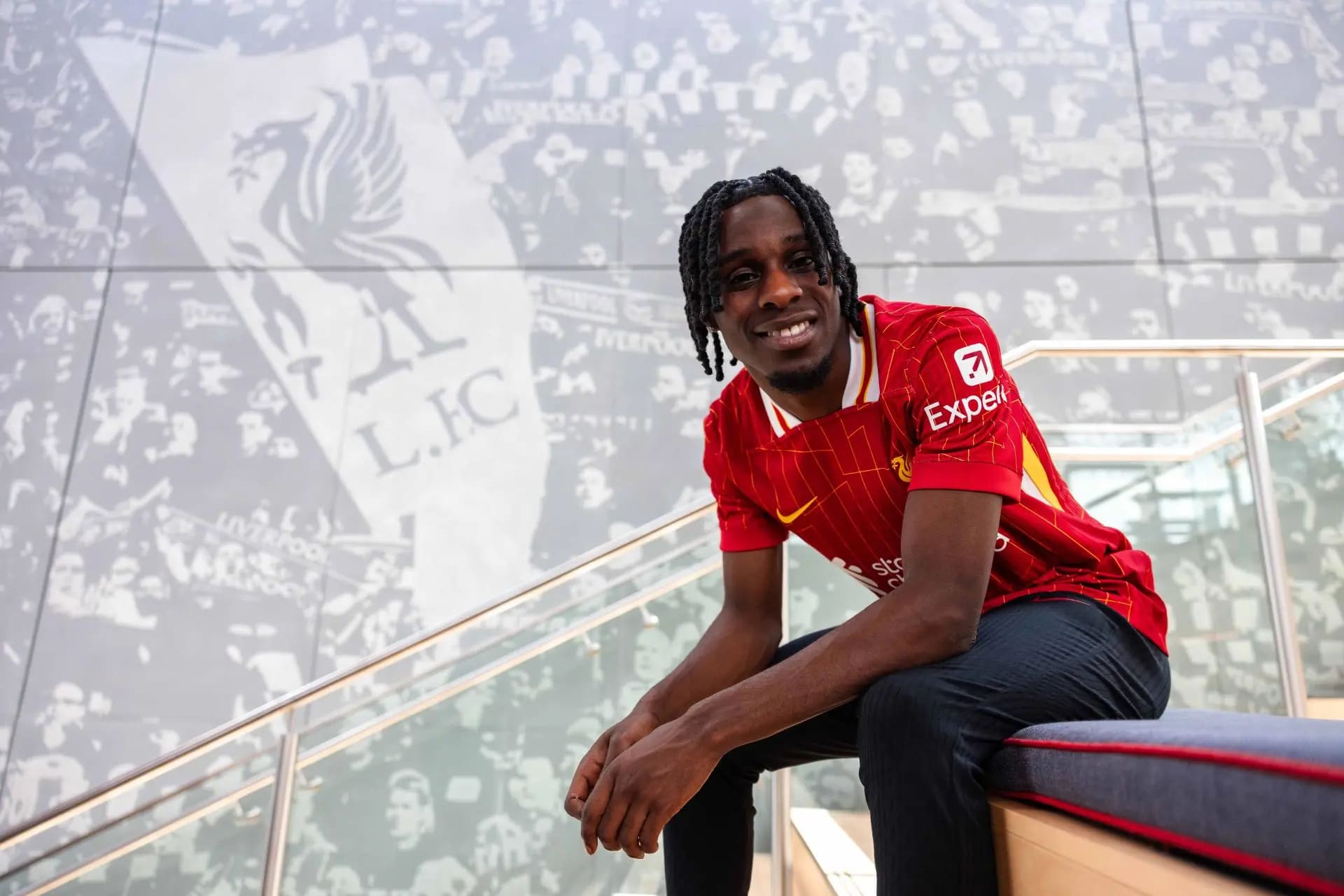 Jeremie Frimpong smiling in a Liverpool shirt after completing his transfer from Bayer Leverkusen