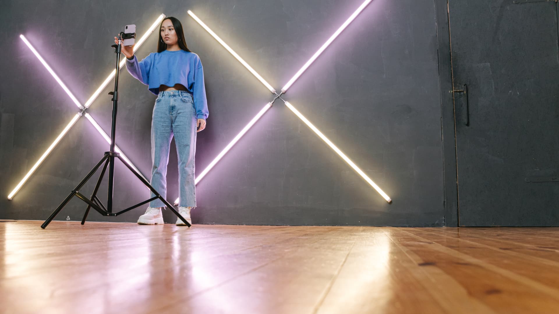 A content creator sets up her smartphone on a tripod in a studio lit with crossed light tubes