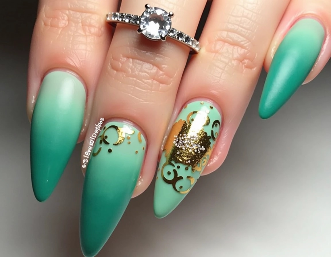 Design a set of long, pointed nails featuring a gradient of green to teal colors, with a matte finish. Incorporate abstract gold foil patterns and a single accent nail with a sparkly, jewel-like texture in the center. Use delicate silver rings with small gemstones on a couple of fingers, and ensure the background is neutral to emphasize the nail art.