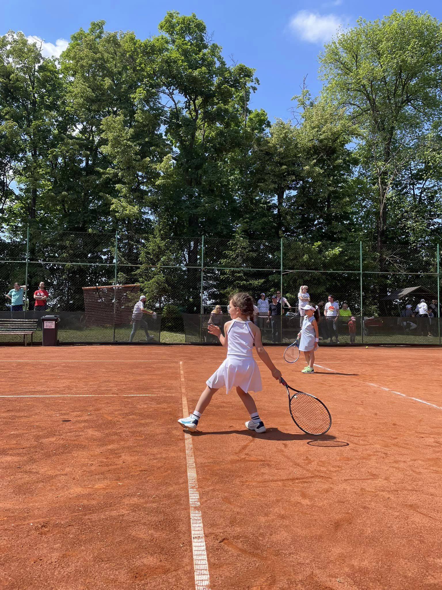 Dievča v bielom hrá tenis na antukovom kurte počas zápasu