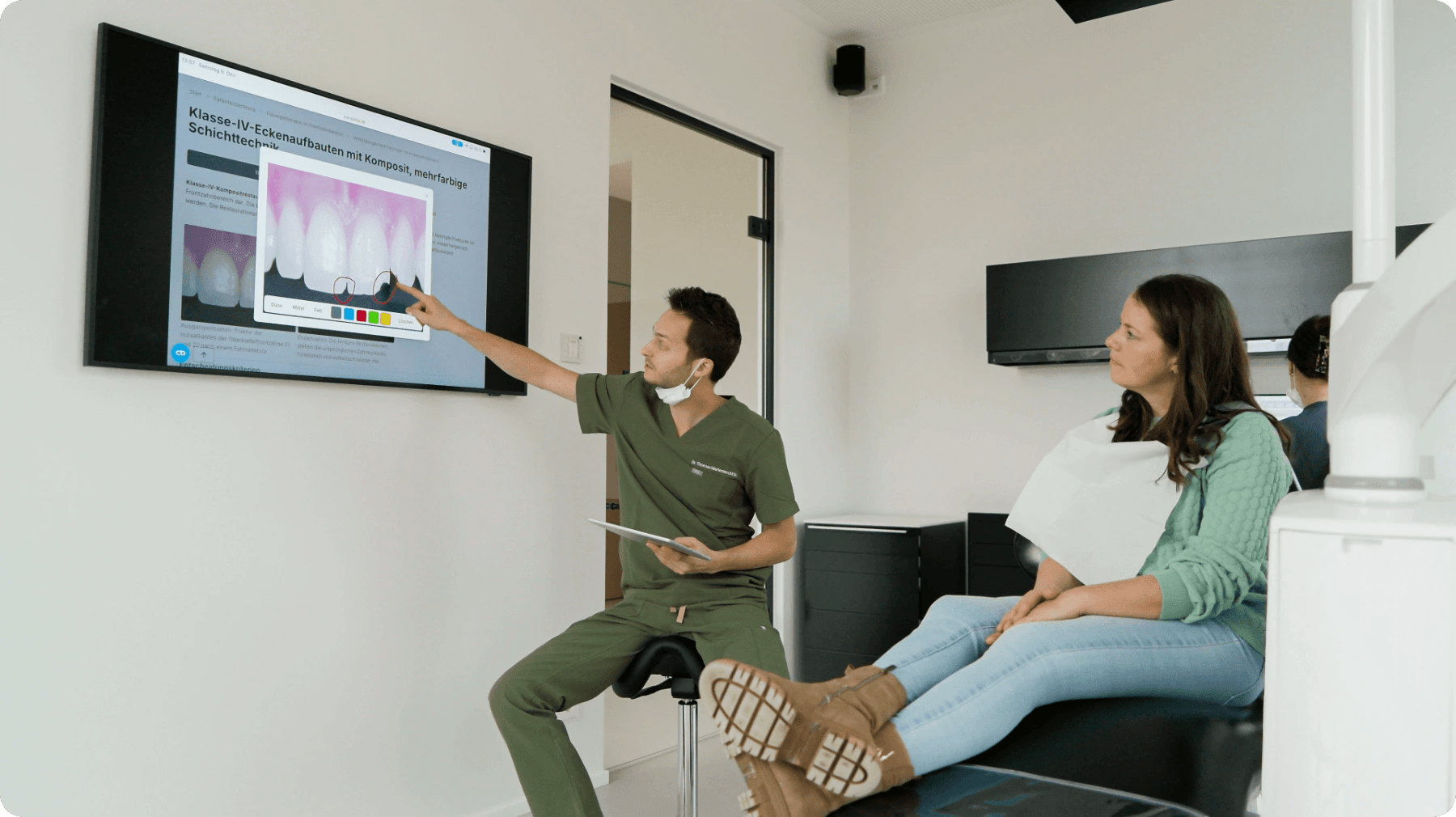 Zahnarzt zeigt auf Bildschirm während der Beratung am Behandlungsstuhl