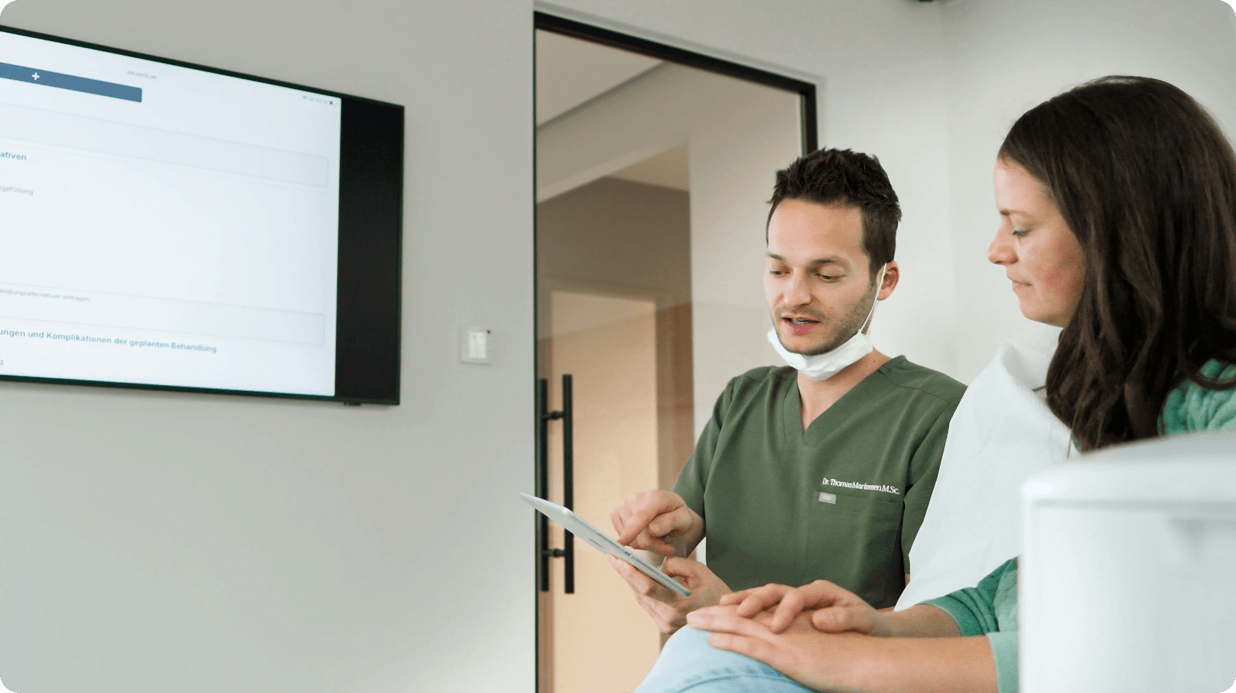 Zahnarzt führt das Aufklärungsgespräch mit Patientin direkt am Behandlungsstuhl mit Tablet