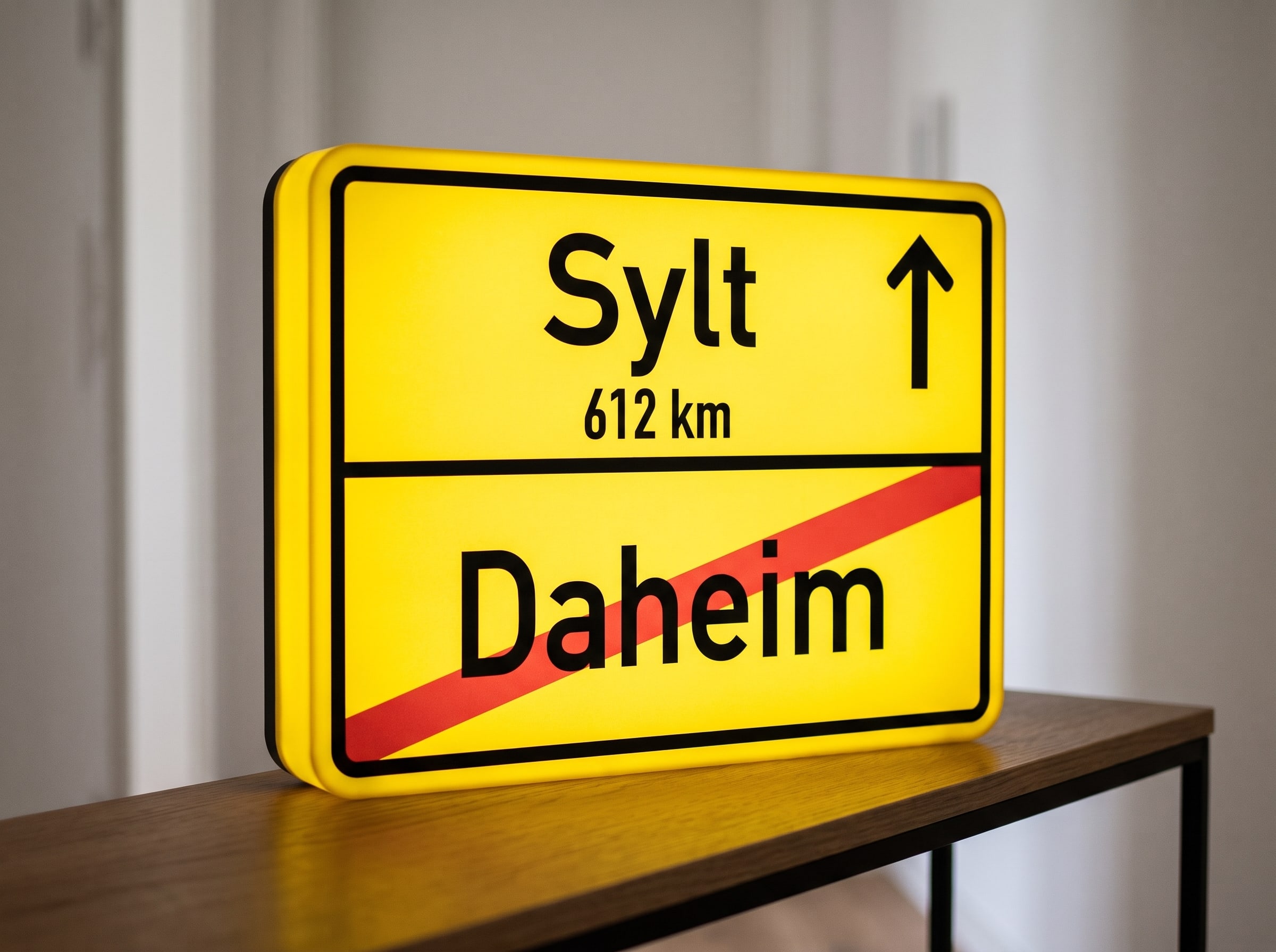 Leuchtende Ortsausgangsschild-Lampe mit Sehnsuchtsziel Sylt und durchgestrichenem Daheim auf einer Konsole im Flur