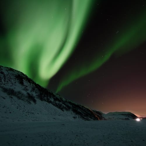 Kuzey Işıkları'nın (Aurora Borealis) muhteşem yeşil ve mor renklerdeki dansı, İzlanda'nın karanlık gökyüzünde.