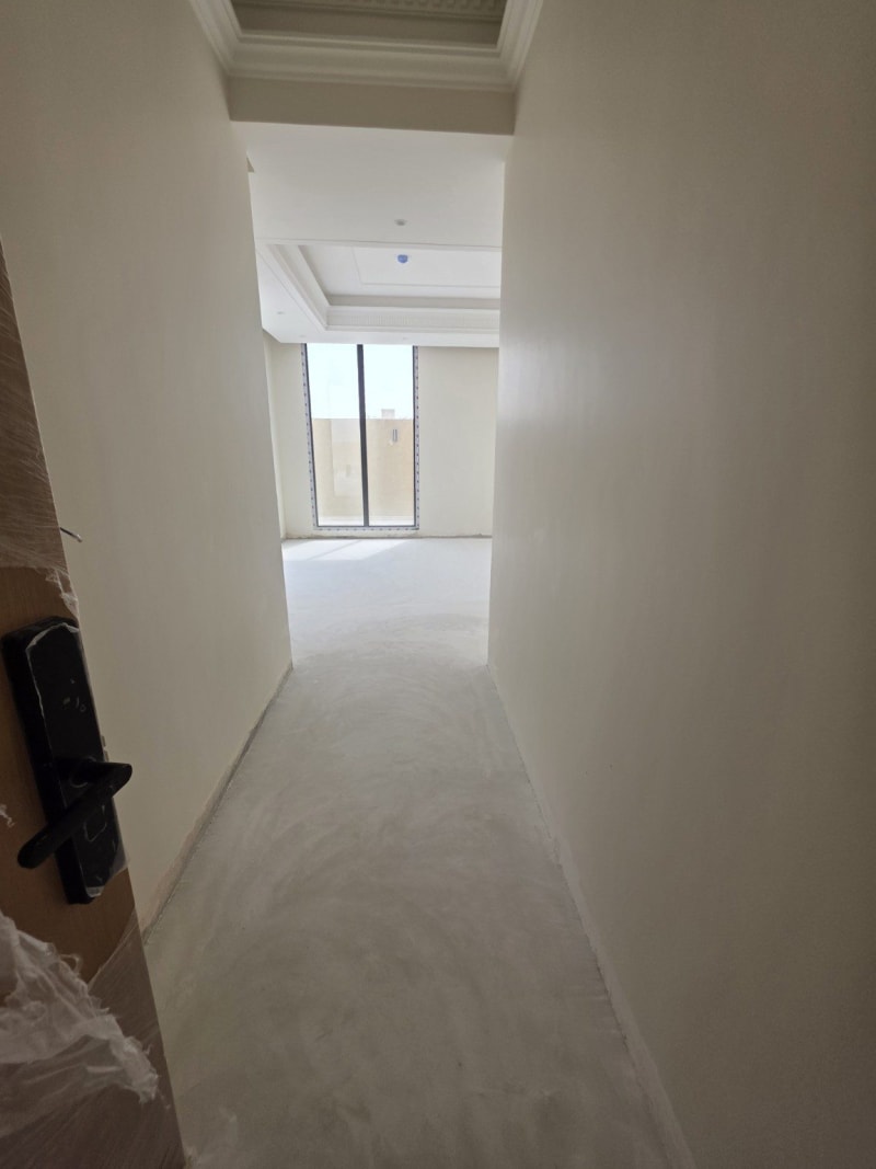 Light microcement floor extending through the studio entrance corridor during installation in Dhahrat Laban