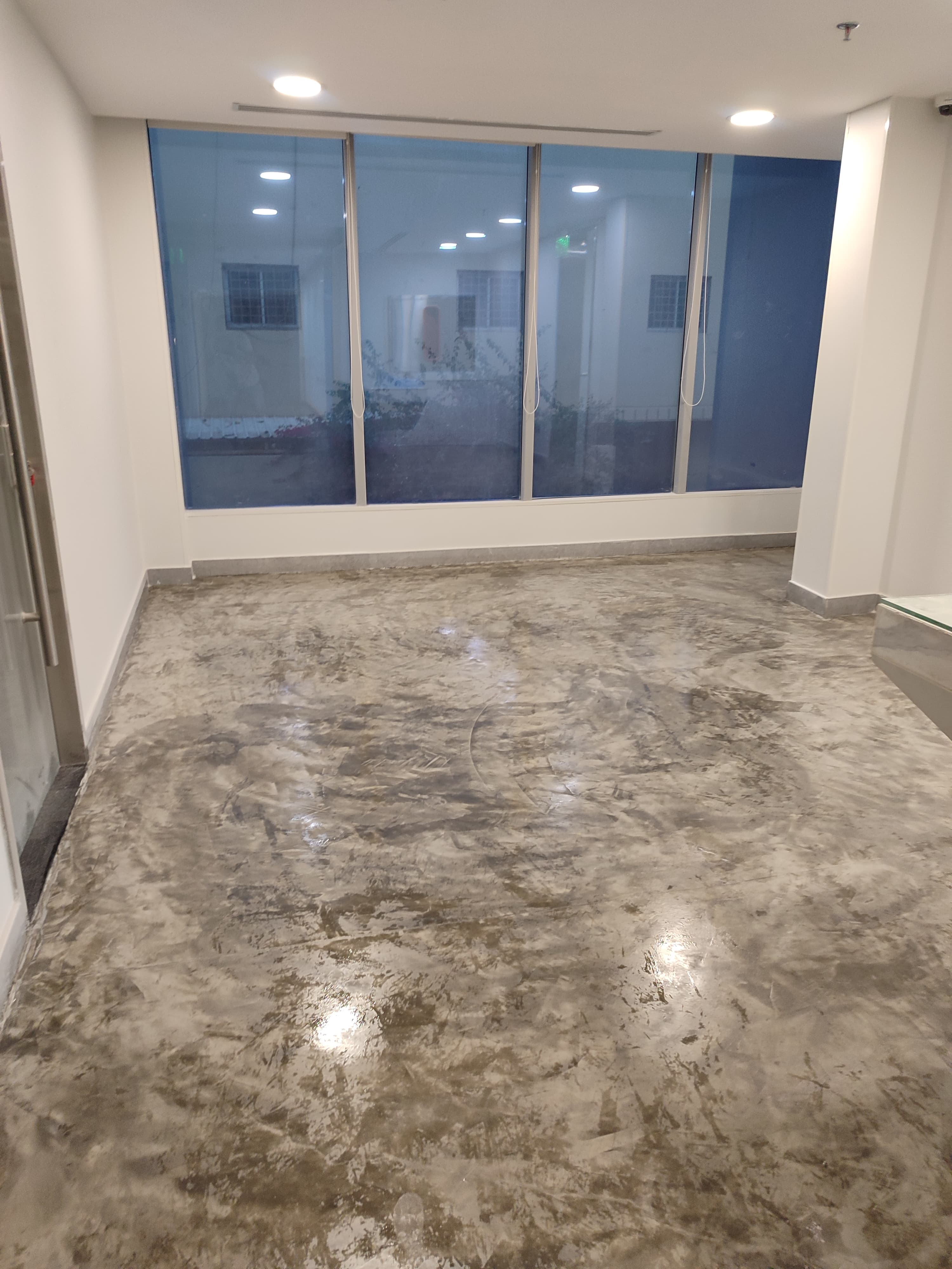 Seamless architectural microcement flooring completed in an open-plan corporate office space with large glass windows in Riyadh, Saudi Arabia.