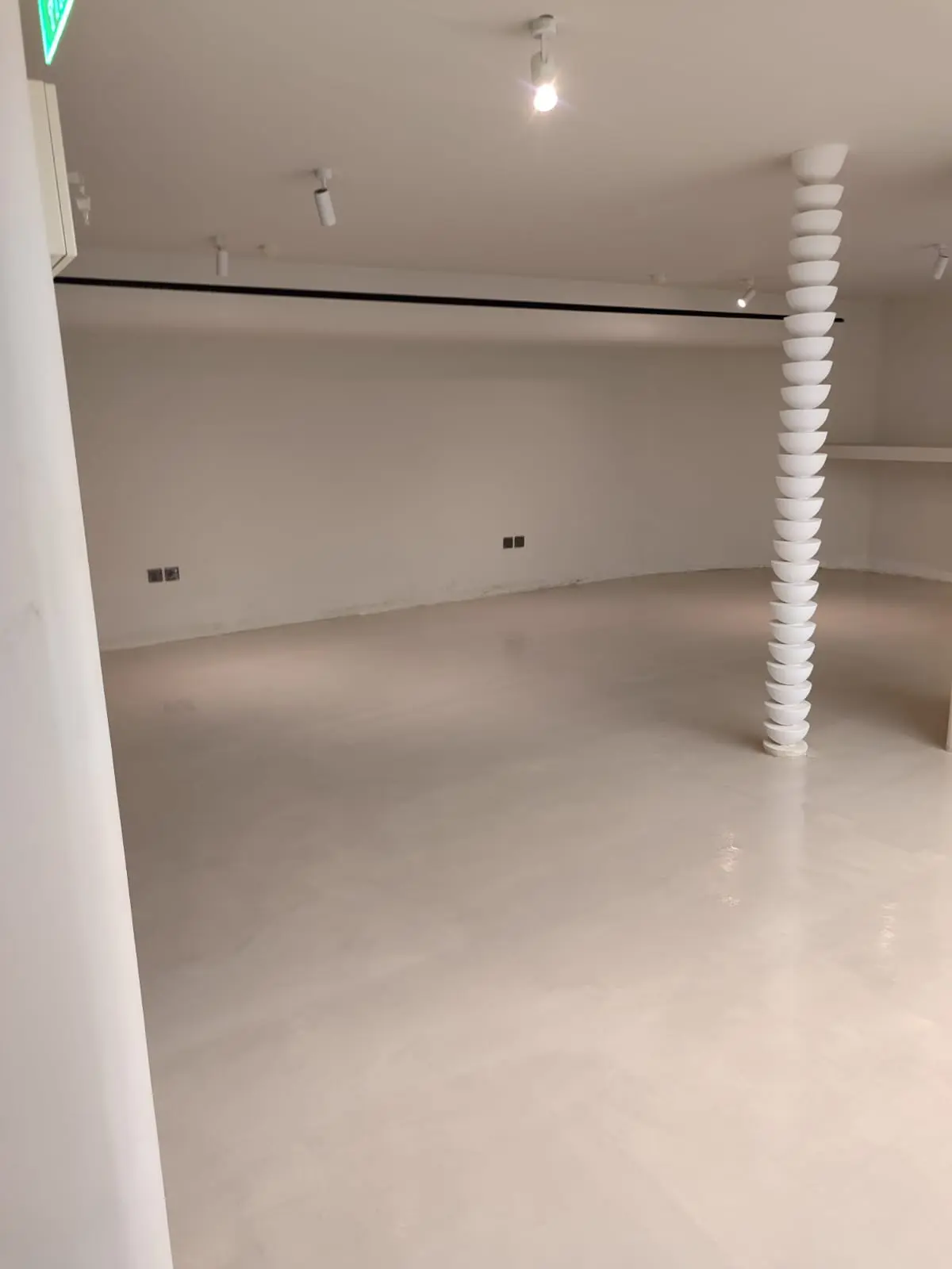 أرضية مايكروسمنت مطفية تغطي مساحة كافيه مفتوحة مع عمود حلزوني منحوت وإضاءة سبوت في الرياض