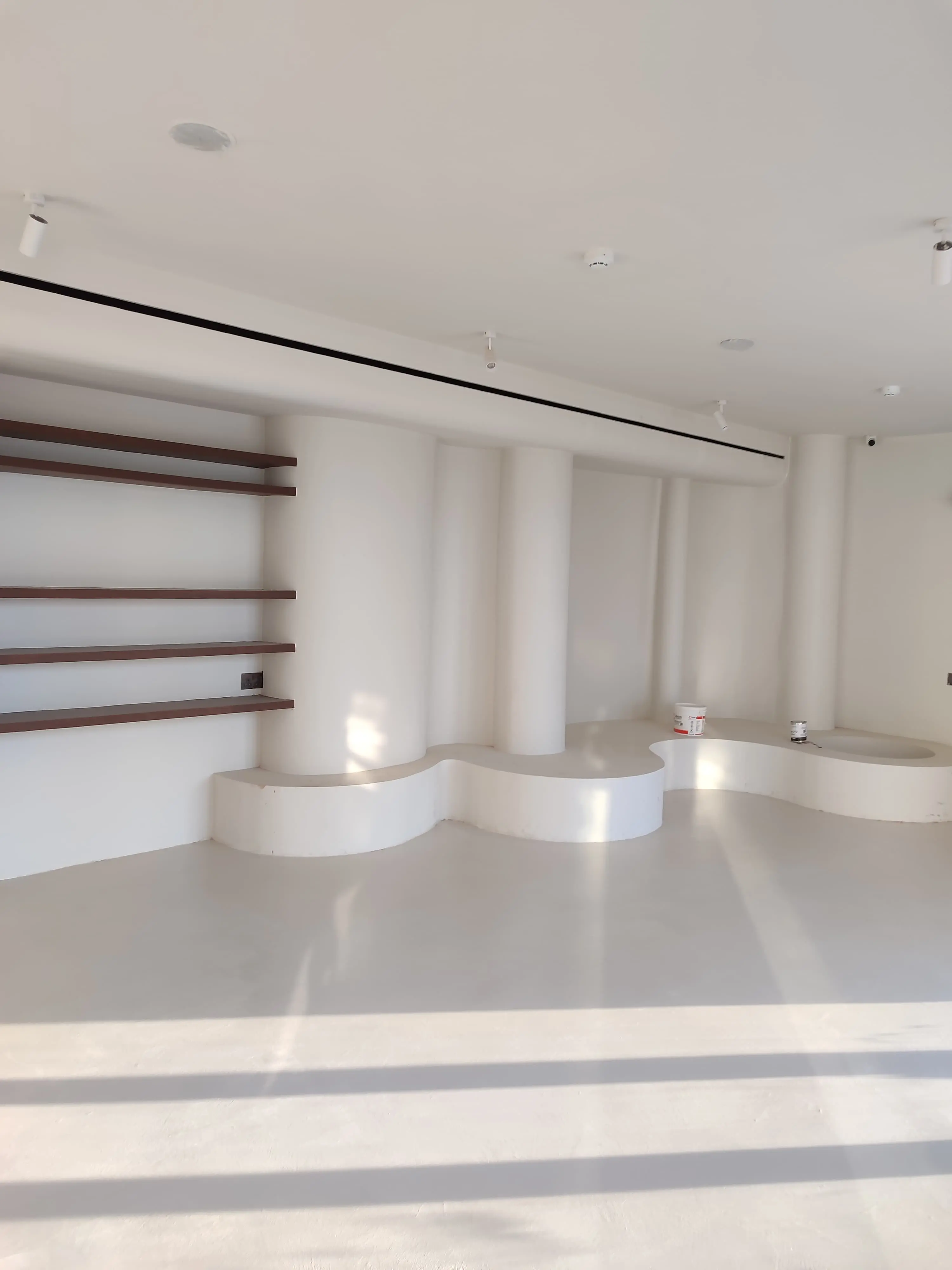 ارضيات مايكروسمنت حول منصات جلوس منحنية مدمجة وأرفف خشبية داخل كافيه قرب برج المملكة الرياض