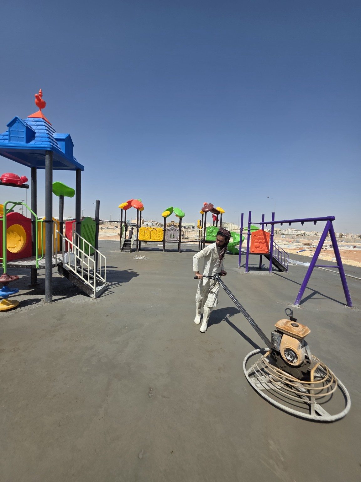 Worker finishing the fresh concrete surface between installed playground structures in As Saadah, Riyadh