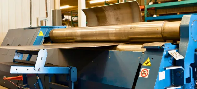 Máquina de calandragem conformando chapas metálicas em formas cilíndricas.