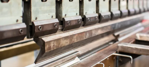 Prensa dobradeira industrial realizando a dobra de uma grande chapa de metal.