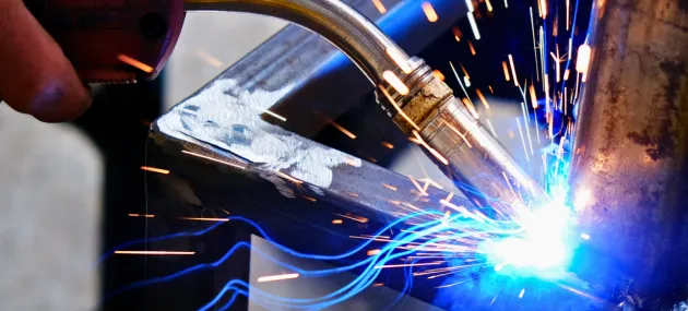 Soldador qualificado realizando solda estrutural em uma grande estrutura metálica industrial.