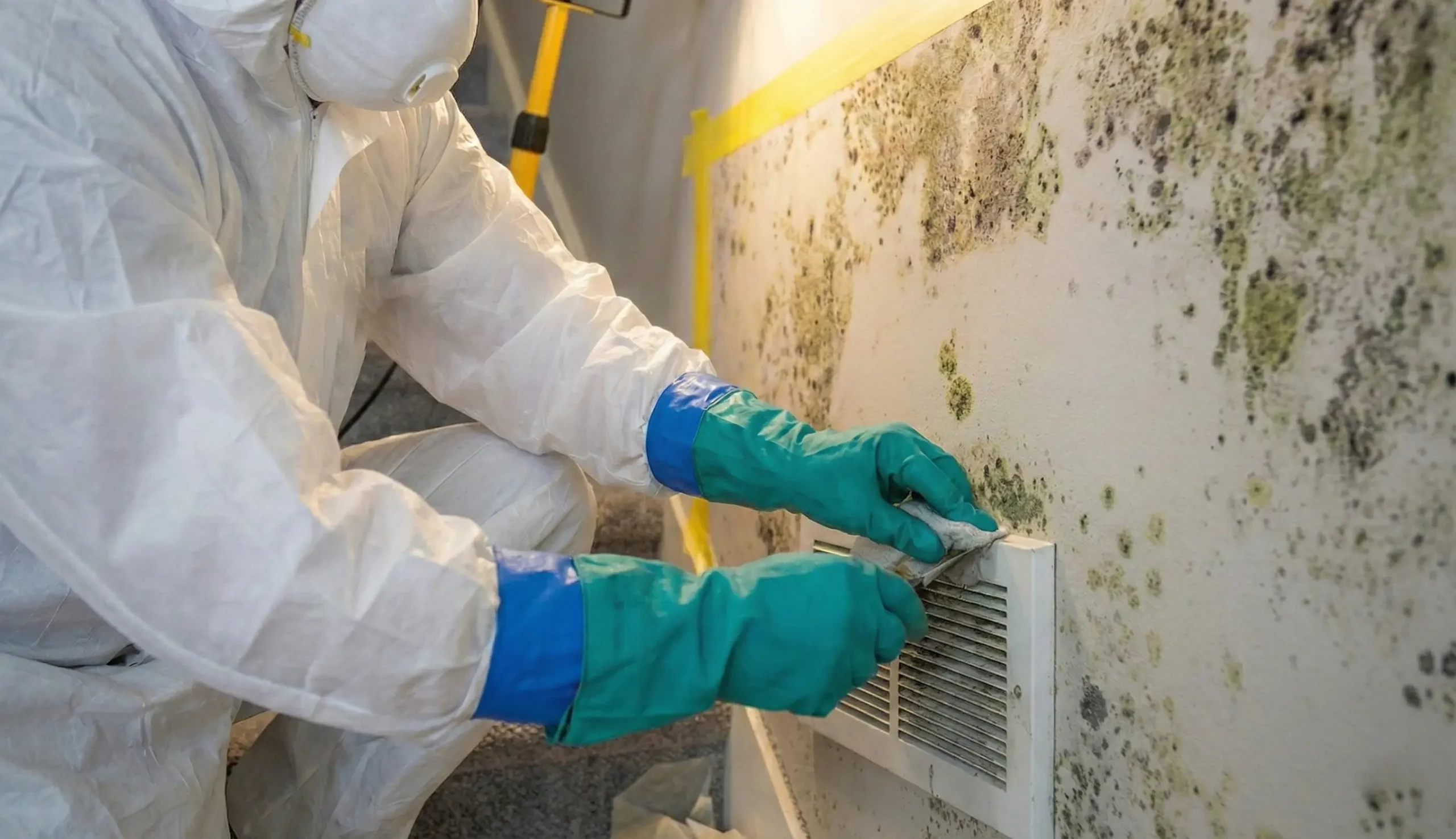 A restoration technician in protective gear treating a damaged wall