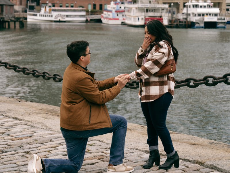 Ring detail photo showing engagement ring on bride's hand with Boston Harbor and city lights blurred in background at twilight