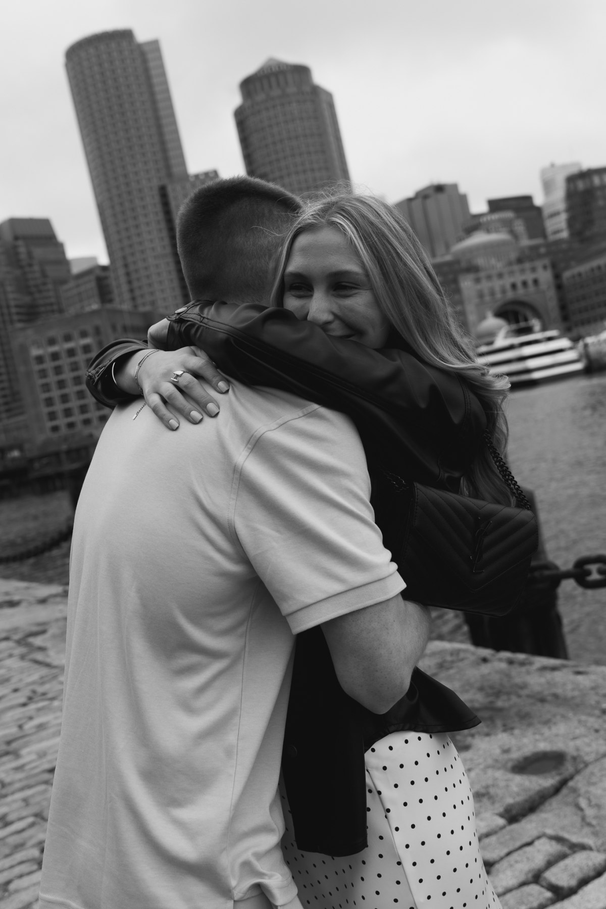 A couple on the Fan Pier waterfront walkway with the Boston Seaport skyline across the channel
