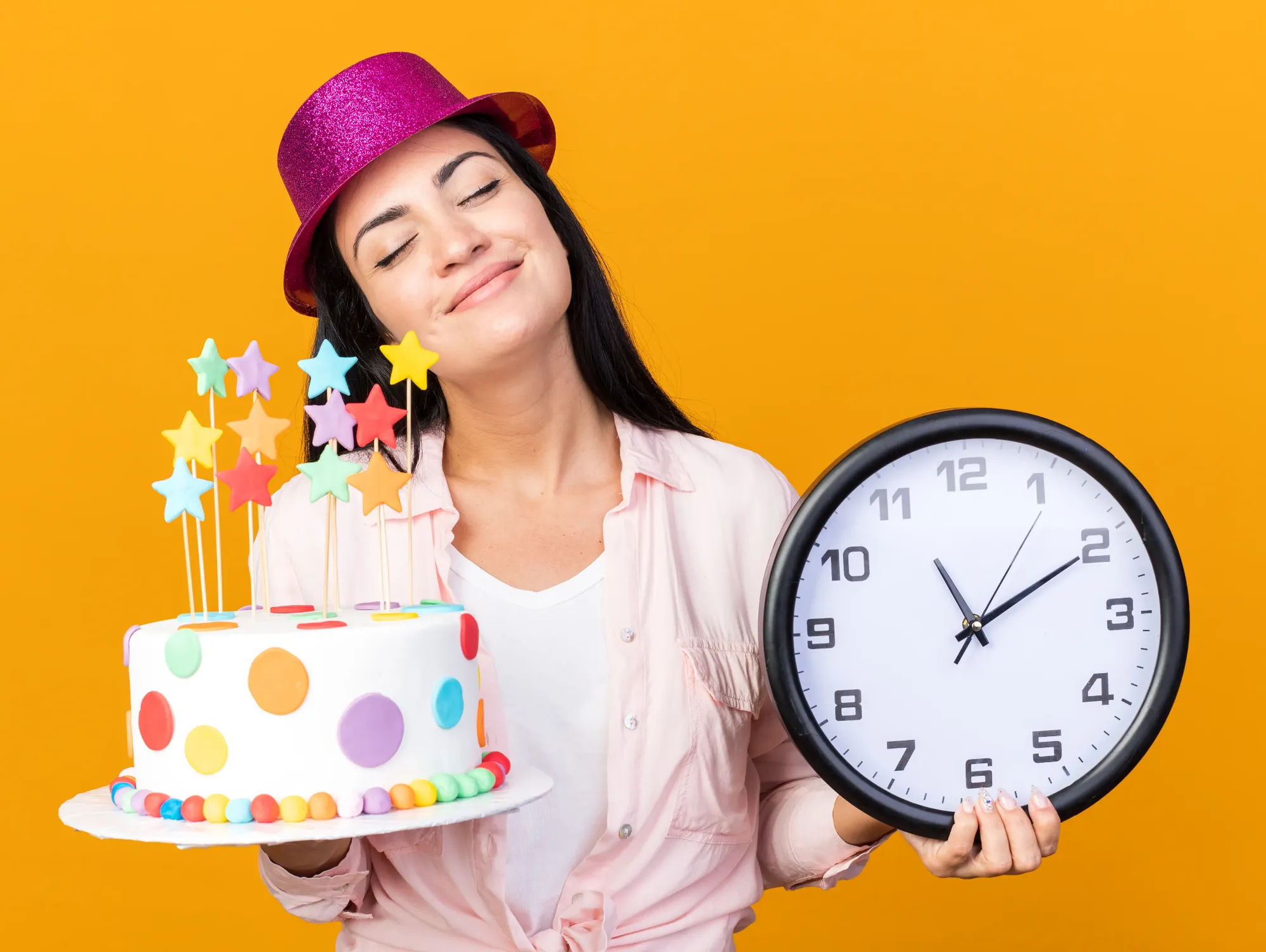A woman in a party hat holding a birthday cake in one hand and a wall clock in the other, the two halves a birthday reminder app handles