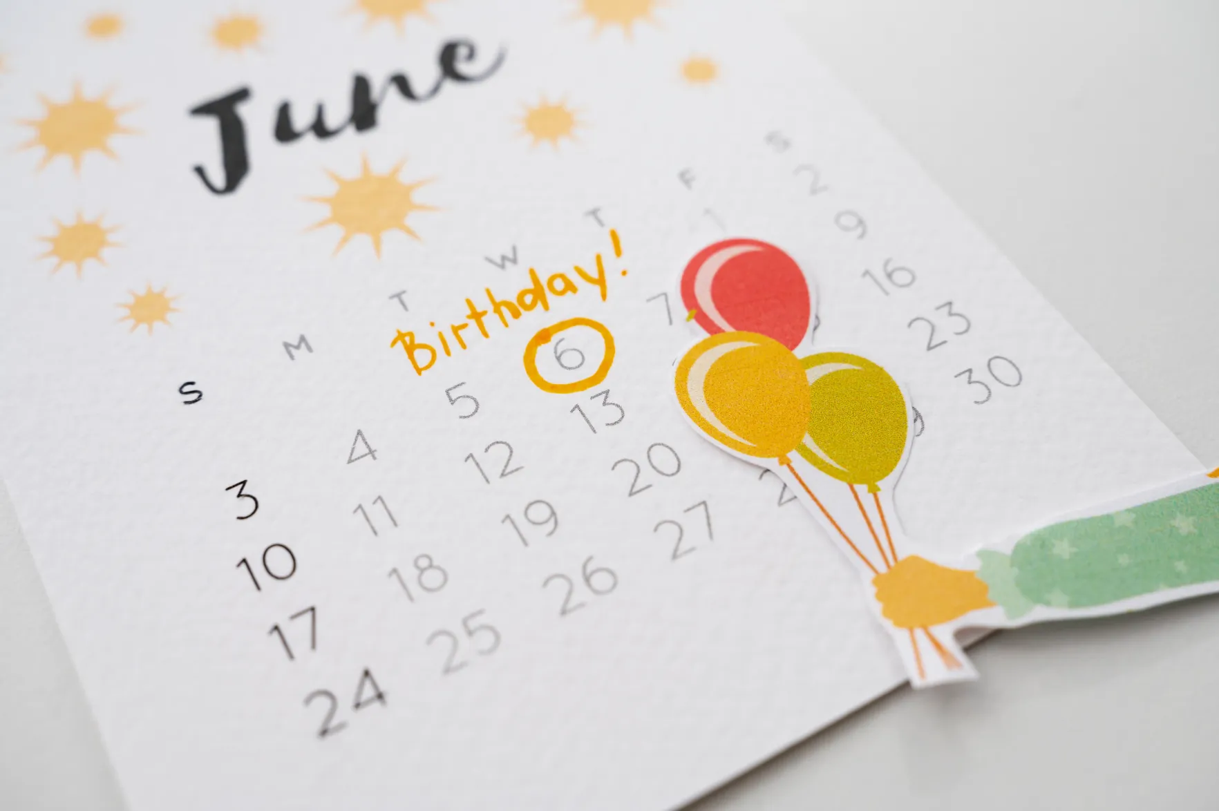 A paper June calendar with the 6th circled in orange and labelled “Birthday!” beside balloon stickers