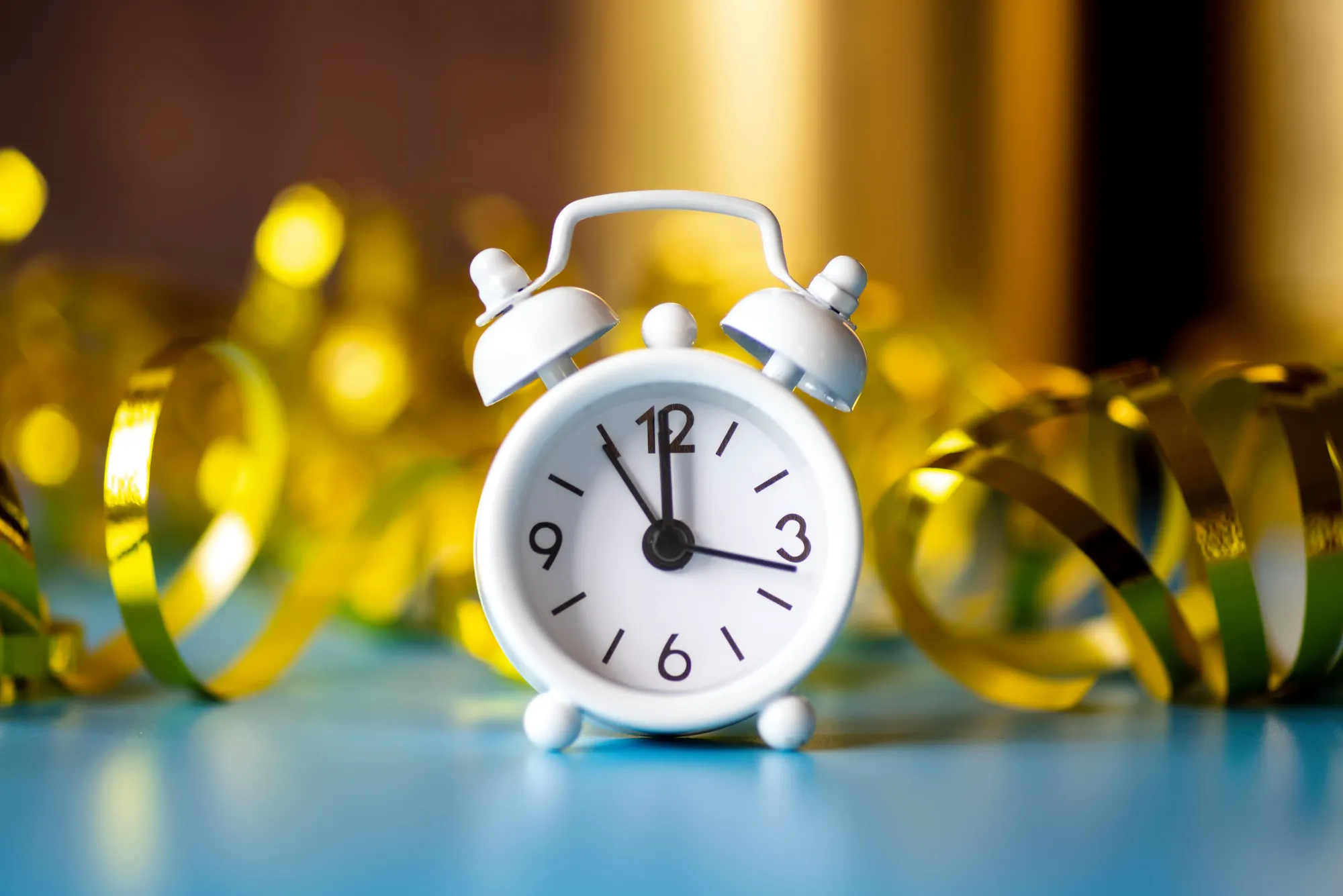 A small white alarm clock standing among curled gold party streamers