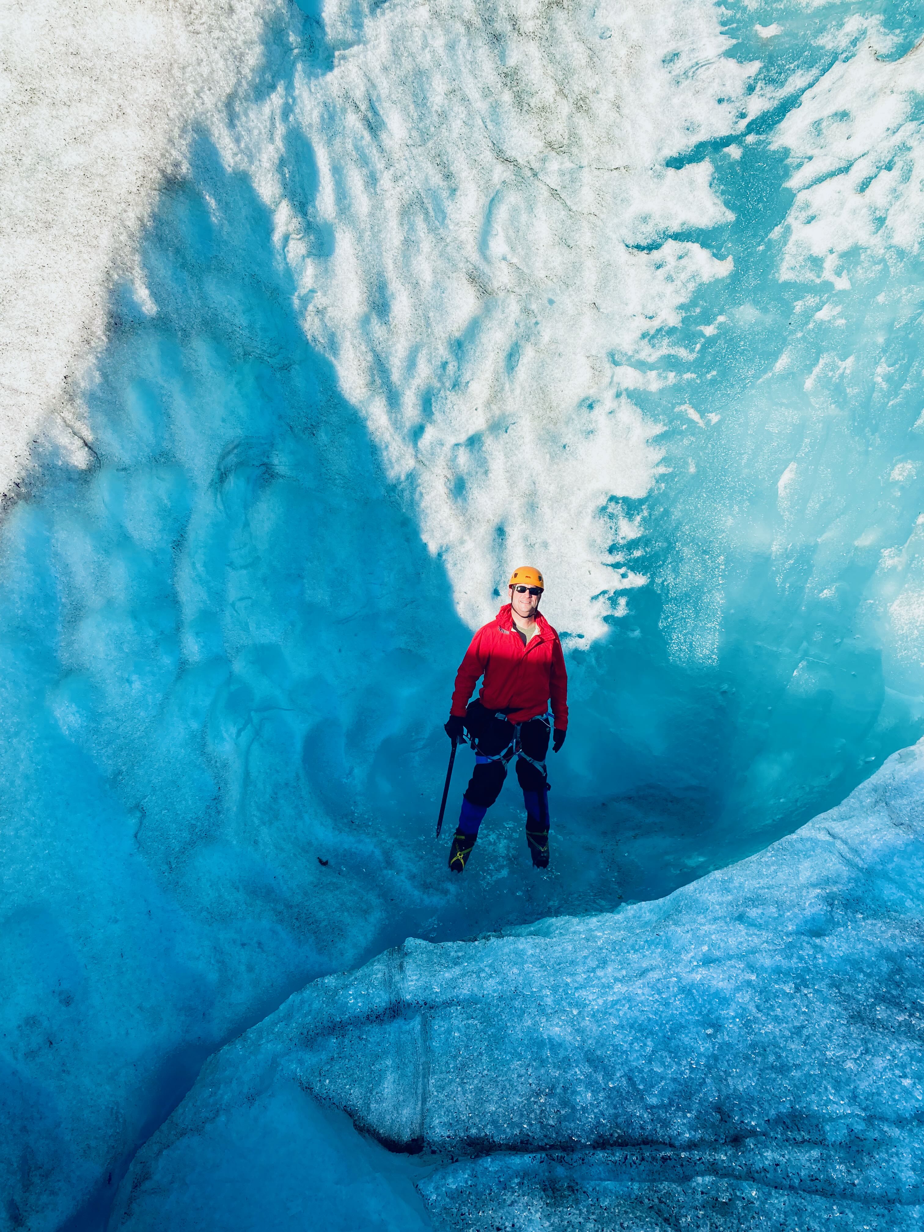 Patrick inside glacial meltwater channel with electric blue ice walls surrounding him