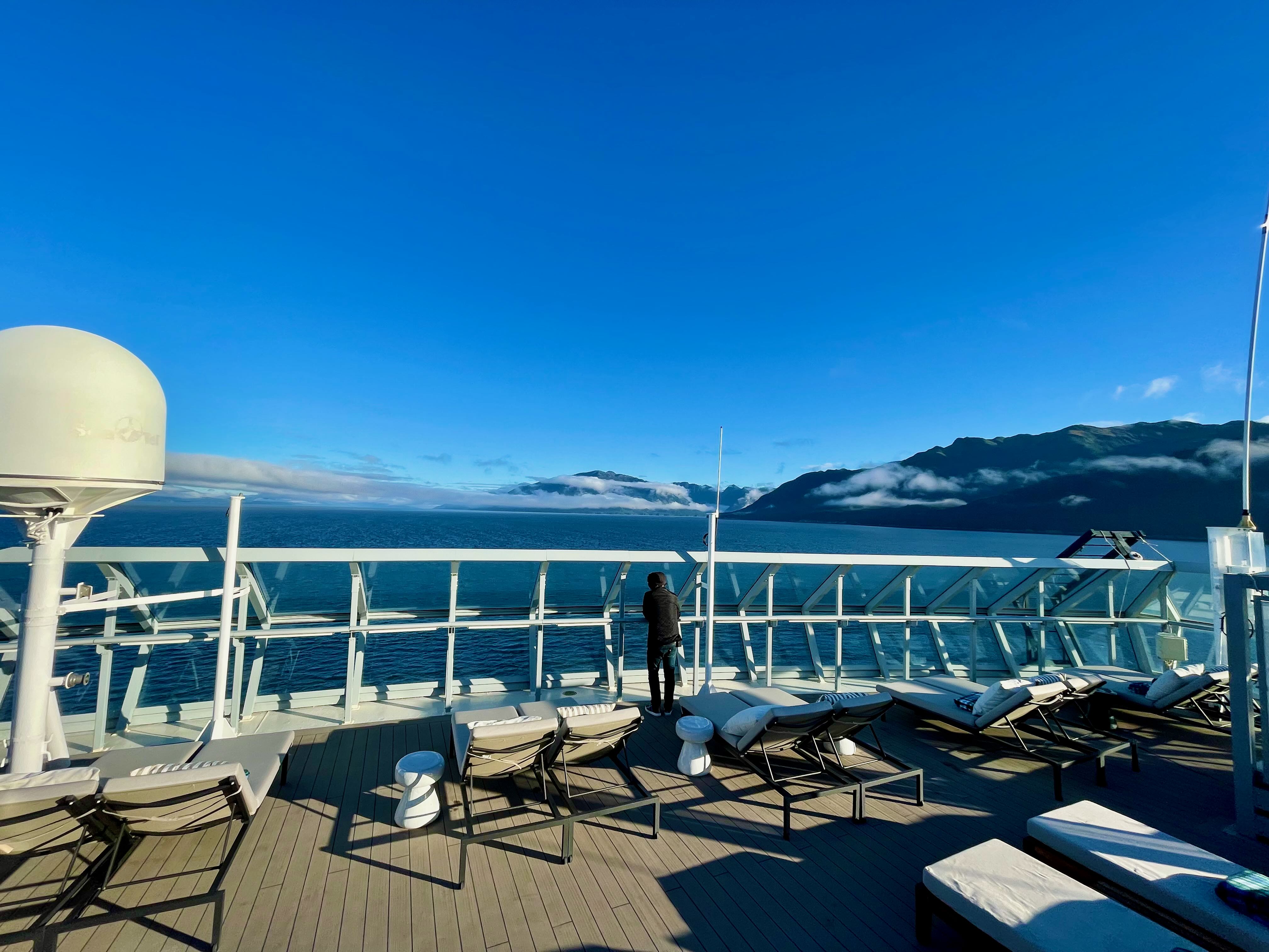 Lone figure at Retreat deck rail with Alaska mountains and clouds behind