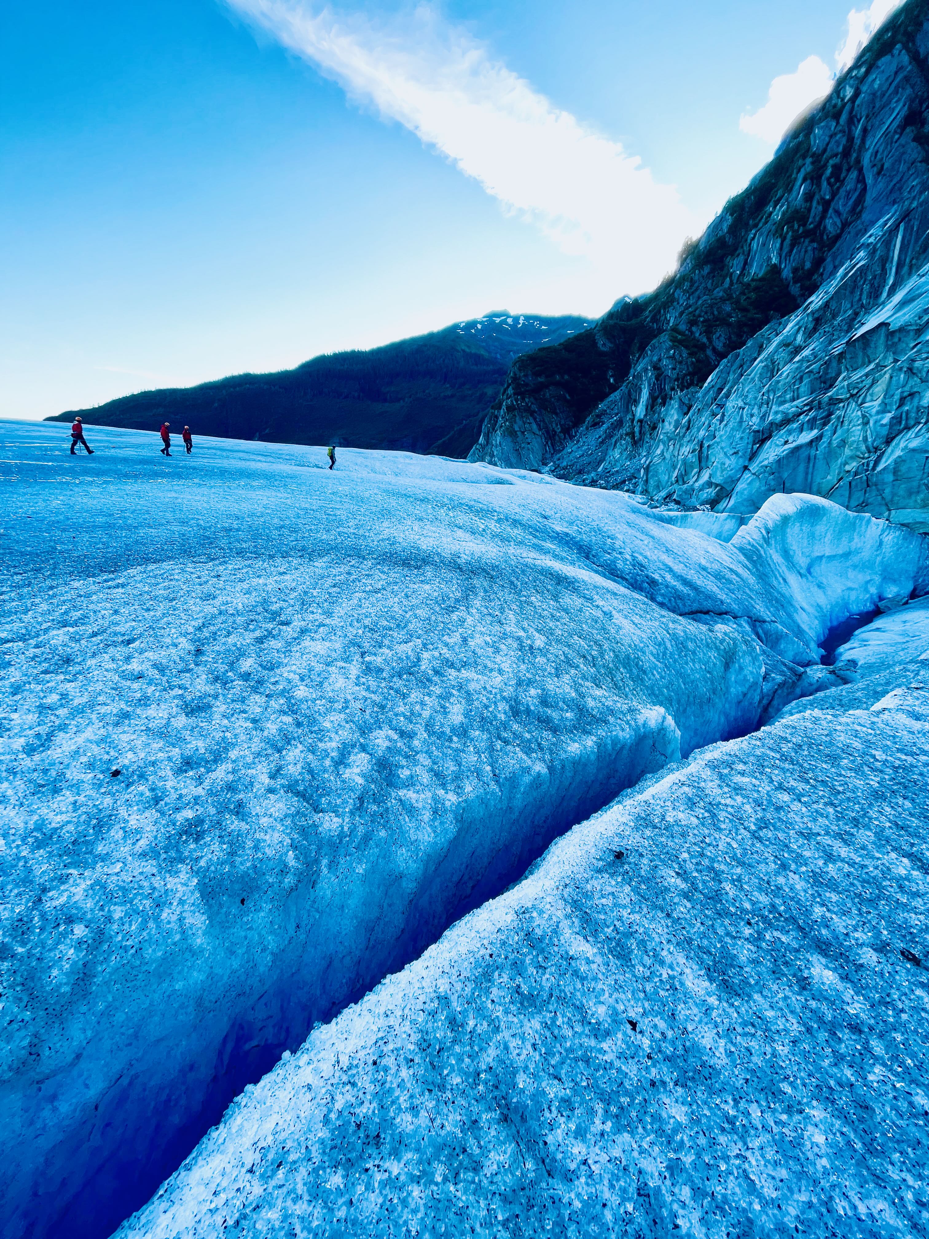 Group trekking with guide navigating meltwater pool on Mendenhall Glacier