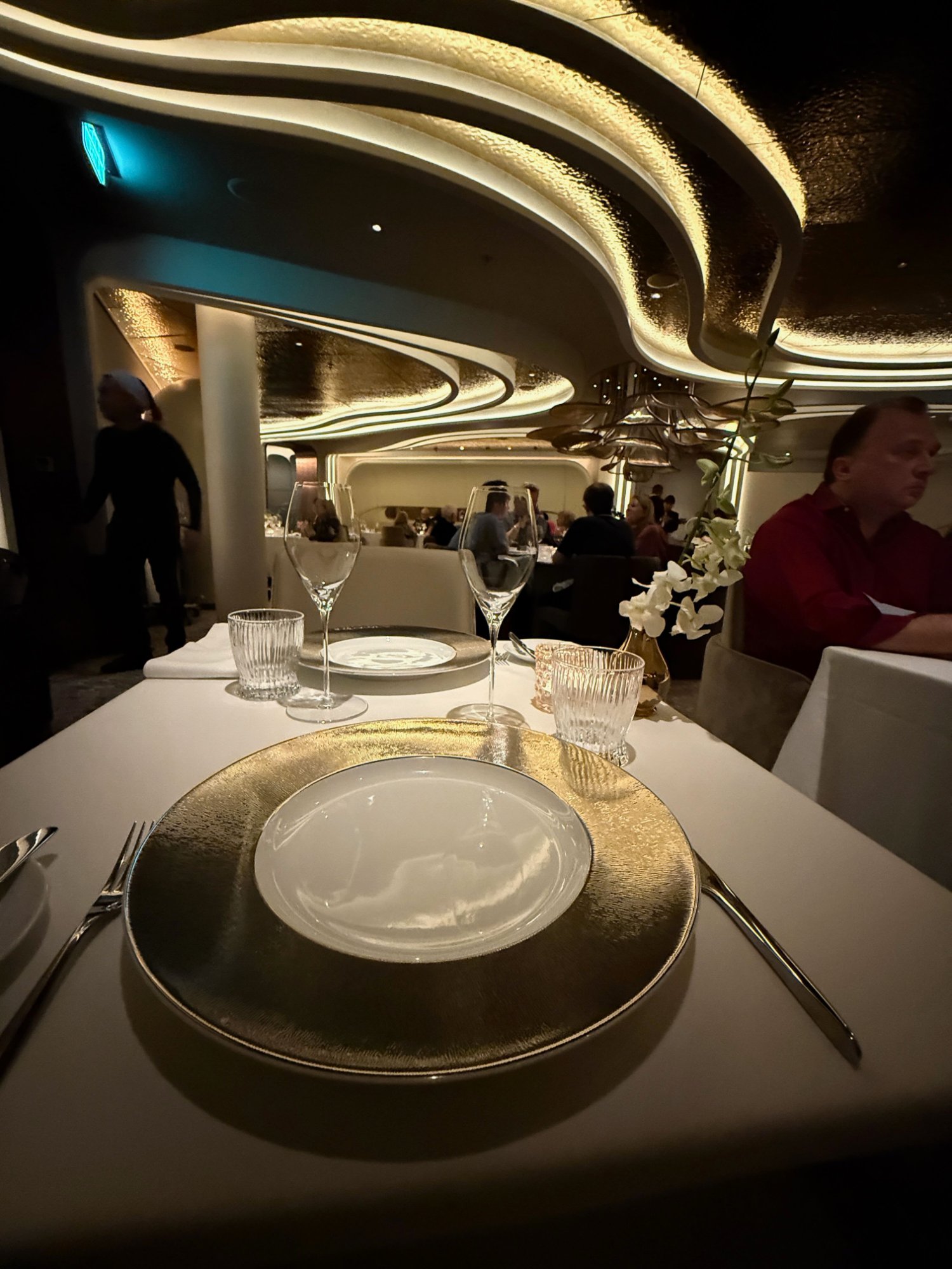 Le Voyage dining room interior — gold wave ceiling, gold charger plates, white orchids