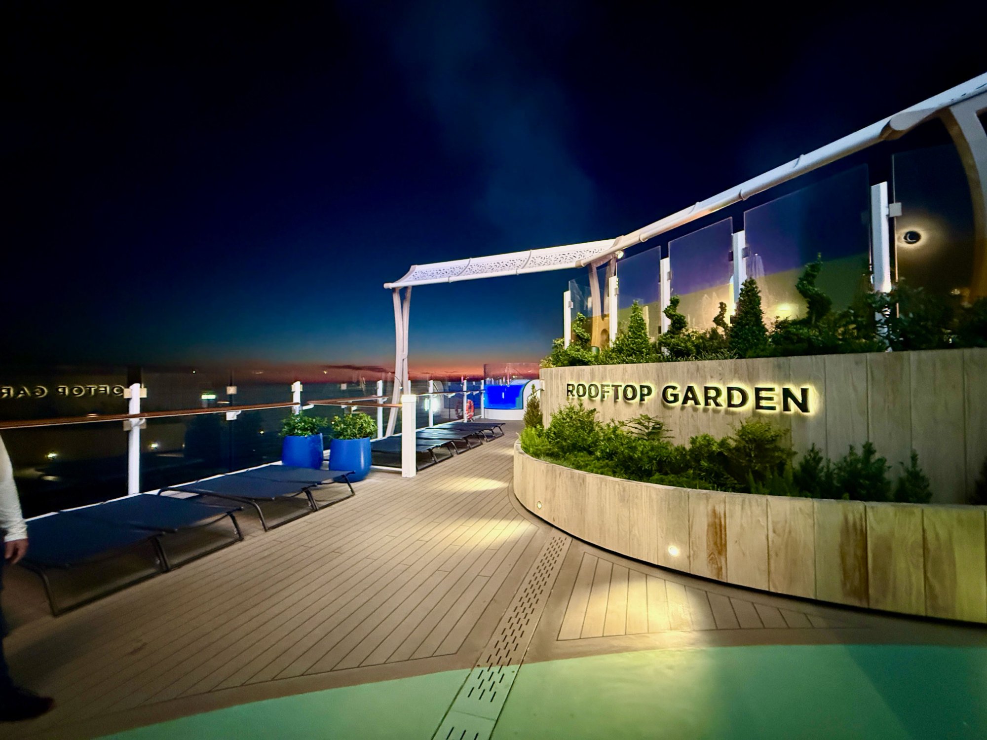 Celebrity Xcel Rooftop Garden at sunset — illuminated signage, deck chairs, orange horizon
