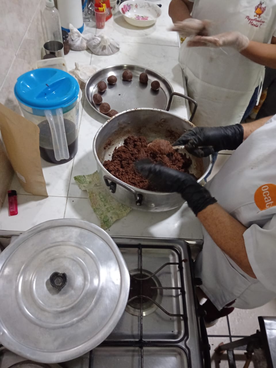 Manos con guantes negros formando la mezcla de chucula en bolas, sobre una olla con la masa restante.