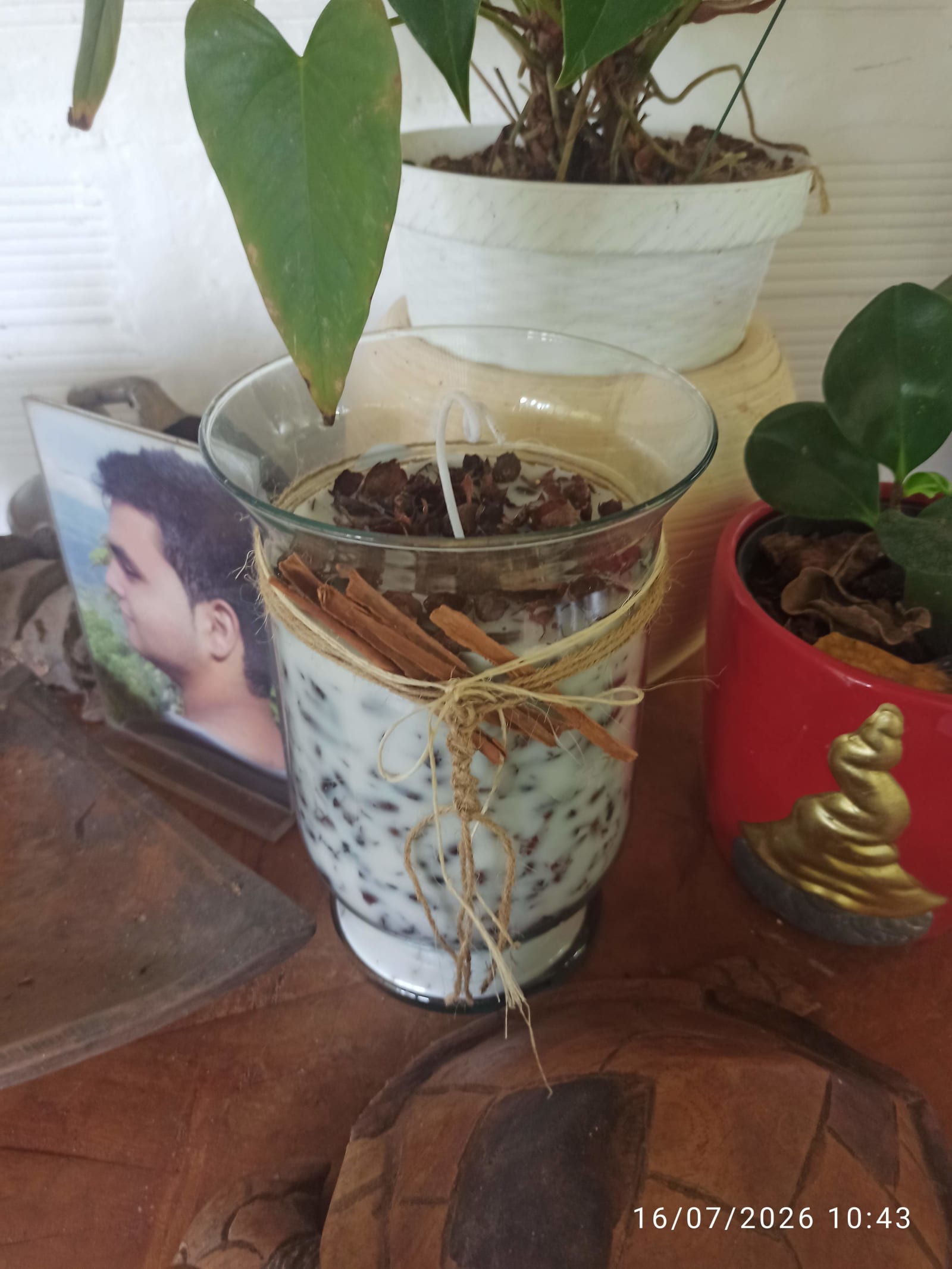 Una vela aromática de cera de soya en vaso de vidrio, con trocitos de cáscara de cacao y astillas de canela amarradas con fibra natural.