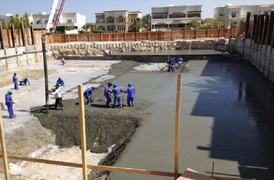 Workers placing and levelling concrete in a deep basement excavation with retained sides at a Dubai villa project