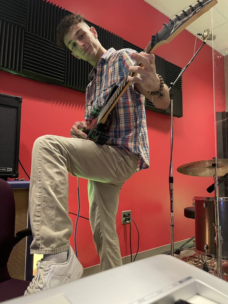 Justin playing electric guitar in his home studio, surrounded by drums, cymbals, and a saxophone