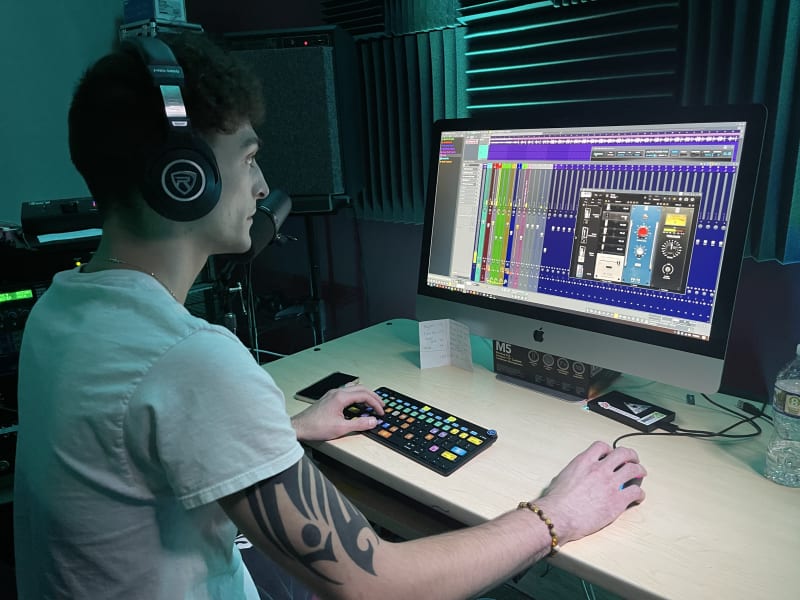 Justin mixing a Pro Tools session on his iMac while wearing studio headphones, forearm tattoo visible