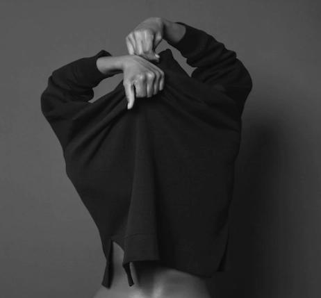 Imagen en blanco y negro de una mujer de espaldas que se está quitando un jersey.
